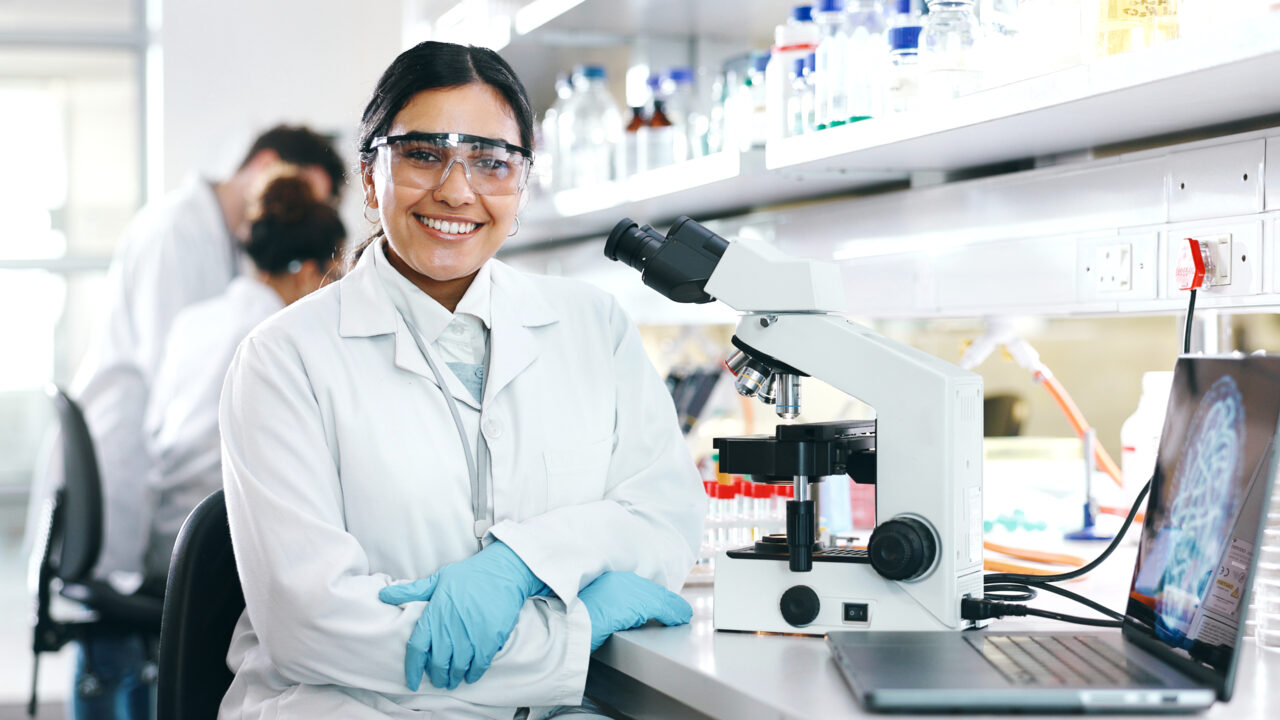 Portrait, science and happy woman on laptop in lab to research chemistry, test or innovation. Microscope, scientist and face of medical doctor in goggles for microbiology, healthcare or pharma study